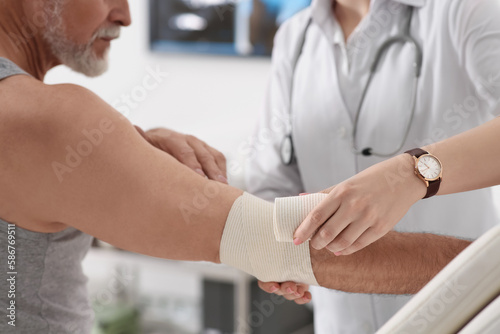 Orthopedist applying bandage onto patient's elbow in clinic, closeup