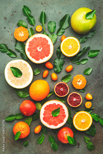 Citrus fruit food background, top view. Mix of different whole and sliced fruits: orange, grapefruit, tangerine and other with leaves on green table