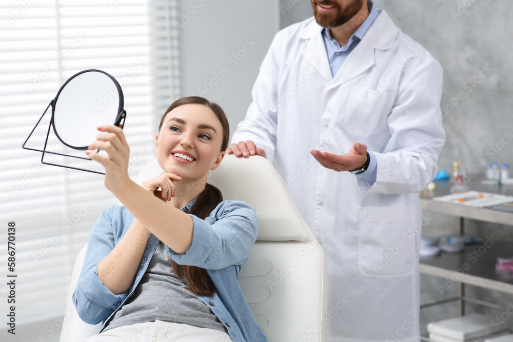 Obraz premium Young woman looking at her new dental implants in mirror indoors