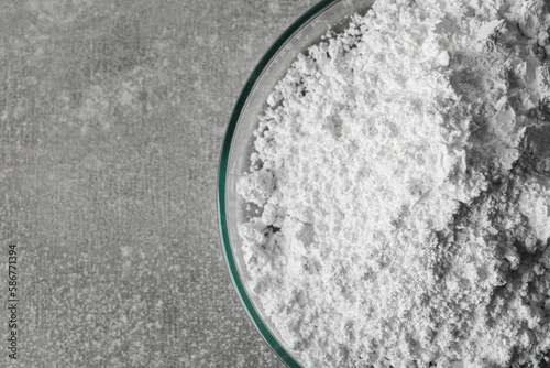 Photography Petri dish with calcium carbonate powder on light grey table, closeup