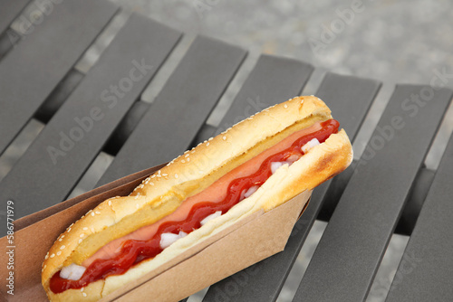 Fresh delicious hot dog with sauce on black bench outdoors