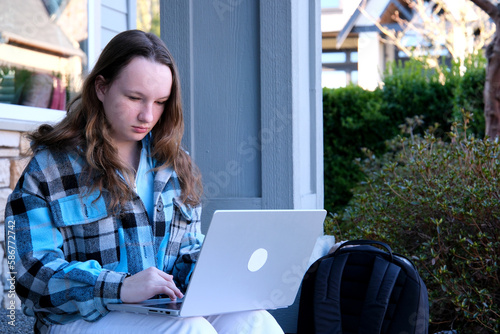 teenage girl with a laptop sitting on the porch of house. She watching the news doing homework online conference backpack folder water bottle pencil ordinary people real life