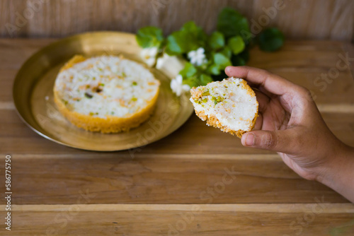 hand holding a piece of Ghewar or ghevar, which is a traditional sweet of rajasthan. It is made of milk, flour, ghee and sugar. Dry fruits and malai cream on top. It is served in brass plate. photo