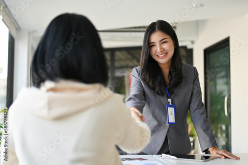 Fotobehang Attractive Asian businesswoman shaking hand with her business client in the office