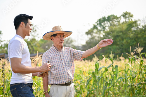 An Asian farmer walking and talking with a male supplier in a cornfield