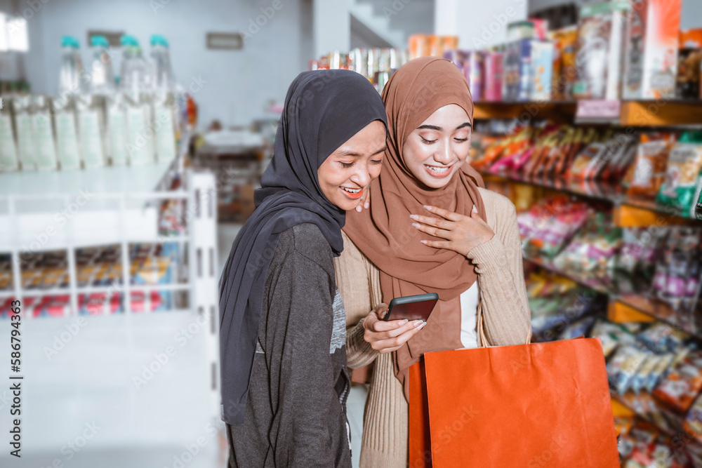 Two Asian Muslim girls using a smartphone while shopping together at the supermarket Two Asian Muslim girls using a smartphone while shopping together at the supermarket