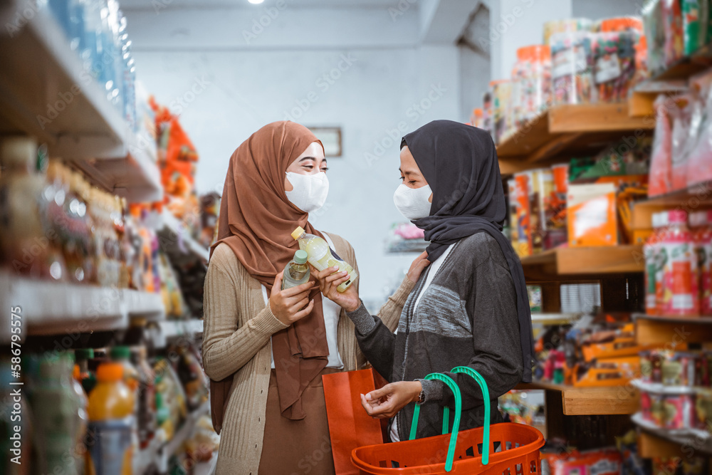 two Muslim girls in masks chatting while shopping together at the store