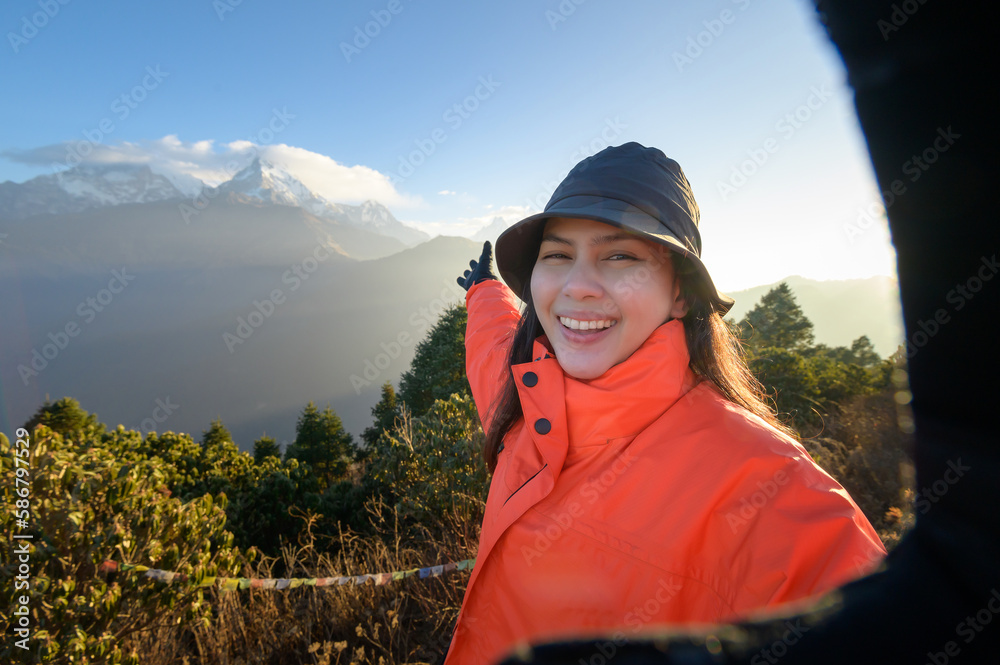 A young traveler takes a selfie or a video call while standing a top a mountain.