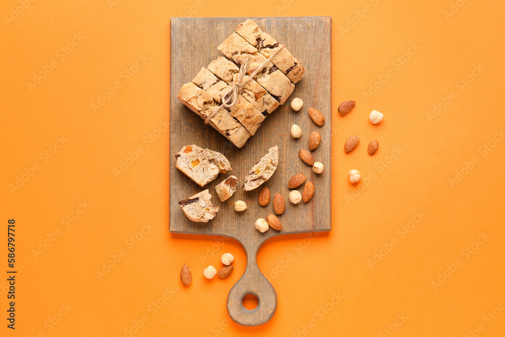 Board with delicious biscotti cookies and nuts on orange background Board with delicious biscotti cookies and nuts on orange background