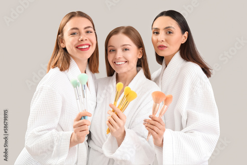 Young women with makeup brushes on grey background