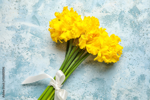 Beautiful narcissus flowers with ribbon on color background