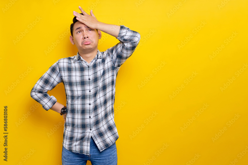 mistaken young Asian man wearing plaid shirt put a hand on his face and fail gesture isolated on yellow background. people lifestyle concept mistaken young Asian man wearing plaid shirt put a hand on his face and fail gesture isolated on yellow background. people lifestyle concept