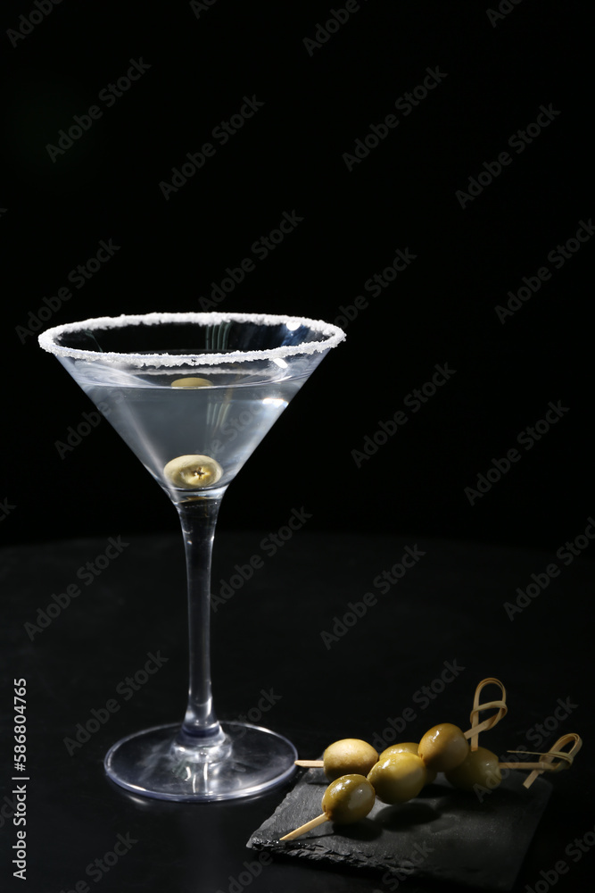 Glass of tasty martini with olives on black background