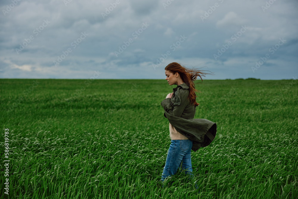 a red-haired woman stands in a green field in rainy, cold weather, holding a raincoat in the wind a red-haired woman stands in a green field in rainy, cold weather, holding a raincoat in the wind