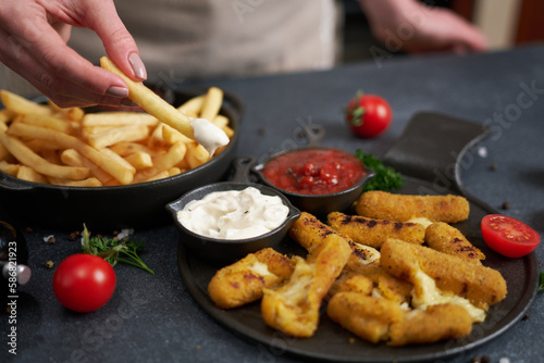 Woman dips french fries into dip sauce with Cheese fried mozzarella sticks on a table