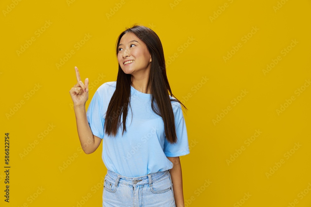 Asian woman smile with teeth hand gestures, signs and symbols on yellow background in blue t-shirt and jeans Asian woman smile with teeth hand gestures, signs and symbols on yellow background in blue t-shirt and jeans