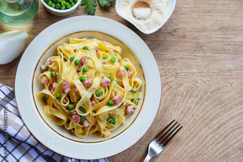 Italian Traditional Dish"Tagliatelle panna,piselli e pancetta",tagliatelle pasta with heavy cream,green peas,smoked bacon,onion,olive oil,parmesan cheeses and peppers on plate with wooden background


