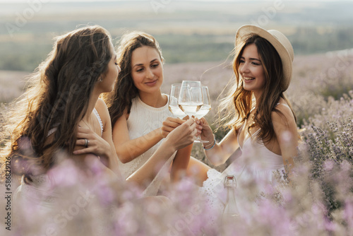 Obraz na płótnie Young and happy woman who enjoys amazing scenery and sunset at picnic. They clinking glasses with wine. w salonie
