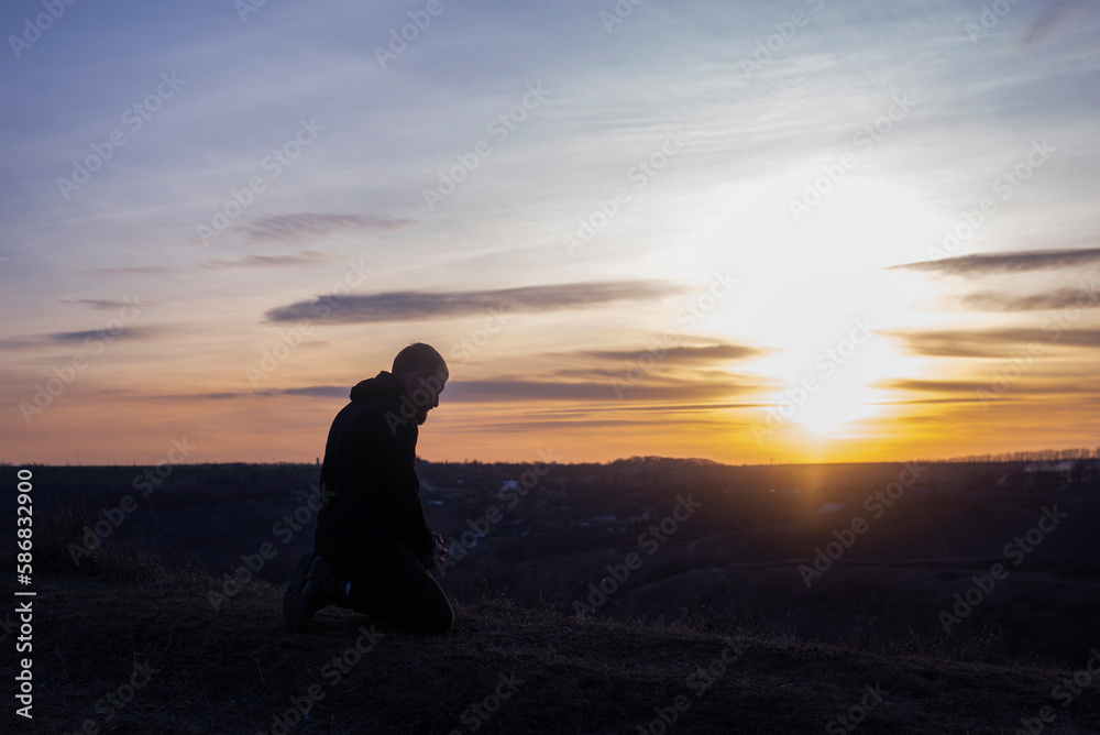 Prayer. Man on his knees praying. Against the background of the sky and sunset. Forgiveness of sins and repentance. Easter Prayer. Man on his knees praying. Against the background of the sky and sunset. Forgiveness of sins and repentance. Easter
