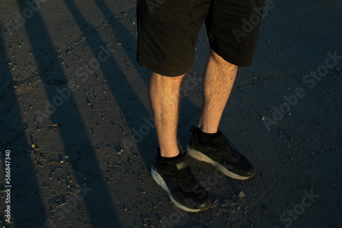 Legs of guy in black shorts and black sneakers. Persons feet stand on ass. Shorts in fashion.