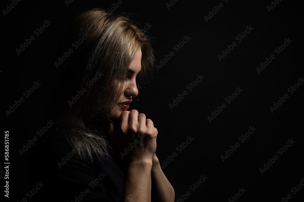 Woman praying with hands together on black background