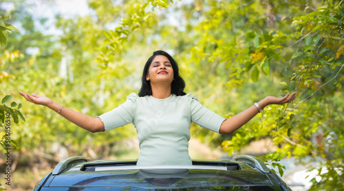 Happy woman feeling nature fresh air by stretching arms on car sunroof - concept of freedom, traveller and refreshment photo