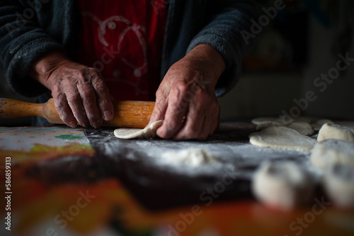 Old female hands at work in the kitchen close up. Grandmother rolls out a piece of dough with a wooden rolling pin. Cooking process. High quality dark photo