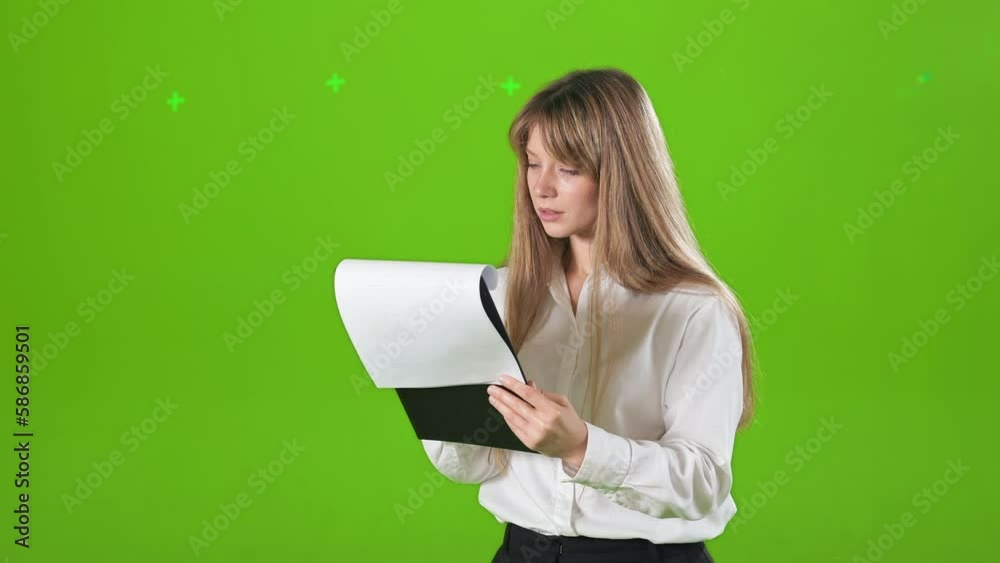 Side view of concentrtaed, focused woman standing, posing indoors in studio. Young, blonde female wearing official clothes, holding folder, reading. Concept of business and work. Side view of concentrtaed, focused woman standing, posing indoors in studio. Young, blonde female wearing official clothes, holding folder, reading. Concept of business and work.