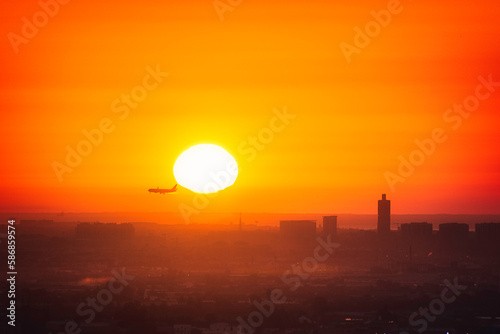 the plane landing and the sun behind it with the cityscape on the background