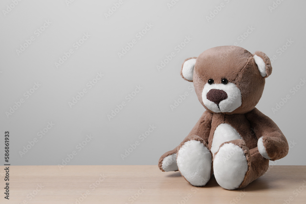 Cute teddy bear on wooden table near light wall, space for text