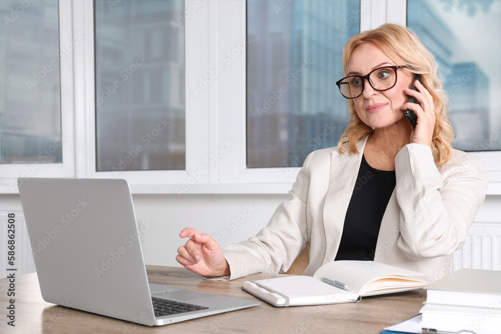 Lady boss talking on smartphone near laptop in office. Successful businesswoman Lady boss talking on smartphone near laptop in office. Successful businesswoman