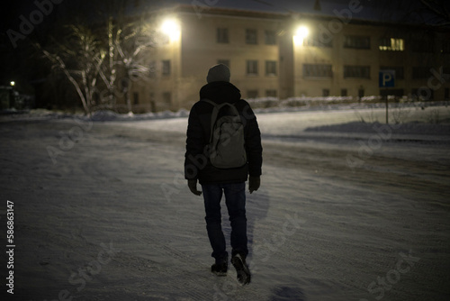 Man walks at night with backpack on street. Guy walking in snow. Details of hike at night.
