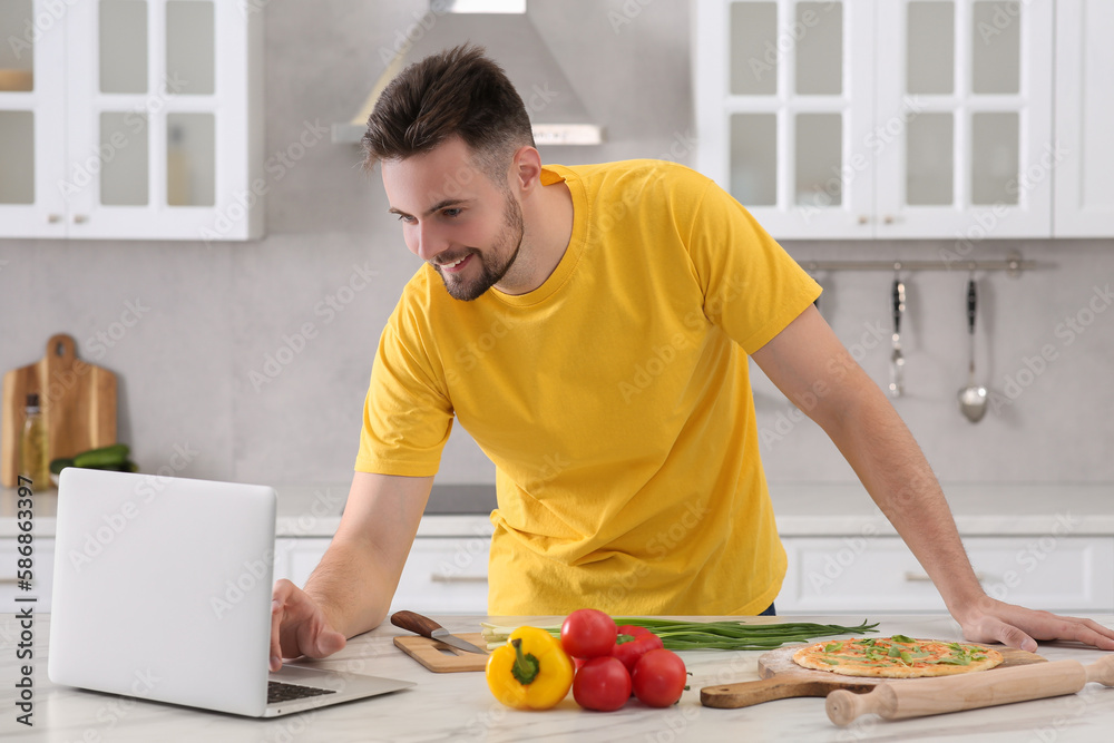 Man watching cooking online course on laptop while making pizza in kitchen. Time for hobby Man watching cooking online course on laptop while making pizza in kitchen. Time for hobby