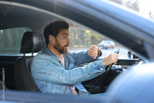Emotional man checking time on watch in car. Being late concept photo