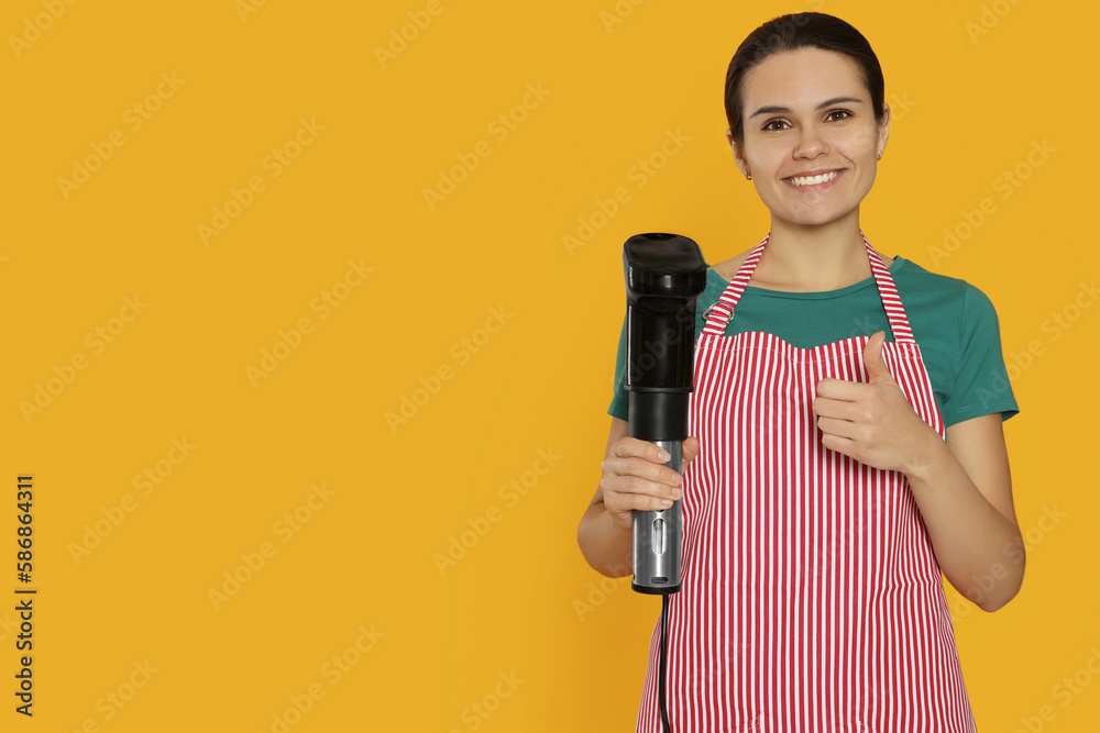 Beautiful young woman holding sous vide cooker on orange background. Space for text Beautiful young woman holding sous vide cooker on orange background. Space for text