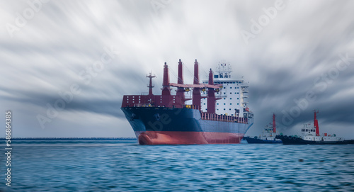 large carrier ship floating in sea, tugboat dragging container ship, stromy sky background motion blur sea in front, mode of transportation concept, photo