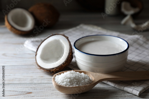 Bowl of delicious coconut milk, spoon with flakes and nuts on white wooden table, closeup