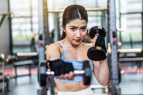 Confident young asian fitness woman doing exercises with dumbbells, Smiling girl doing sports indoors with dumbbells lifting weights. Fit fitness girl in sportswear exercising inside to slim down.
