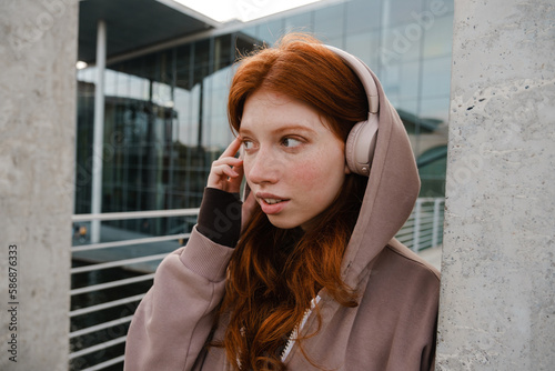 Young girl listening music with headphones and looking aside while standing outdoors