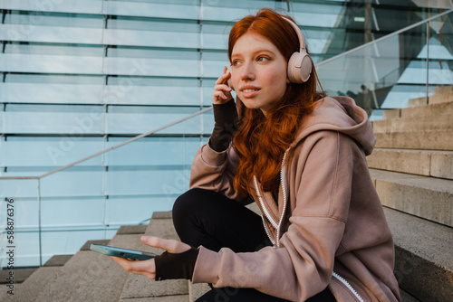 Portrait of pretty girl listening music with haedphones and mobile phone while sitting on stairs photo