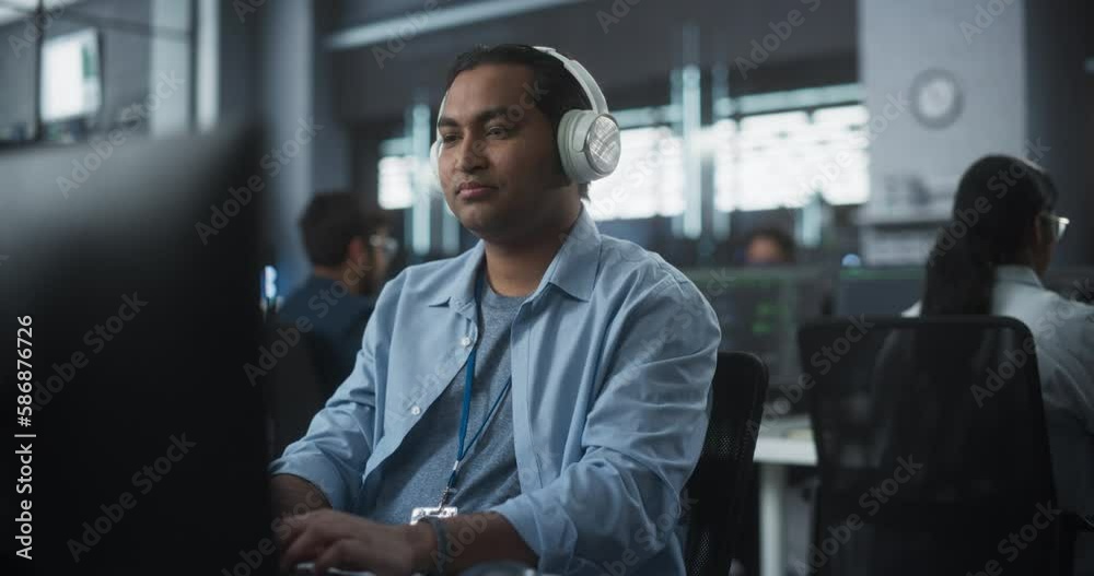 Indian System Administrator Working in a Research E-Business Facility on a Desktop Computer. Focused Software Developer in Casual Clothes Wearing Headphones and Updating Server System Database Indian System Administrator Working in a Research E-Business Facility on a Desktop Computer. Focused Software Developer in Casual Clothes Wearing Headphones and Updating Server System Database
