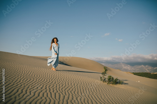 Woman with long hair in a stylish dress poses in the desert sands.