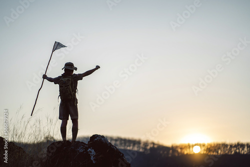 Silhouette of a boy standing on a rock raising his hands rejoicing in success.