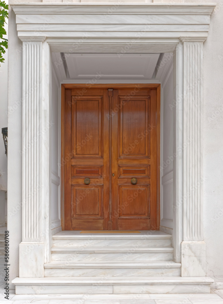 A simple, yet luxury house entrance with a solid wood door and white marble decorated walls. Travel to Athens, Greece.