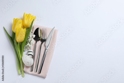 Cutlery set  Easter eggs and beautiful flowers on white background  flat lay with space for text. Festive table setting