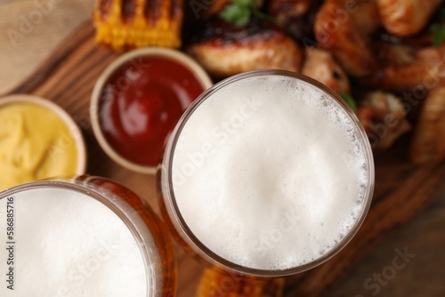 Glasses with beer, delicious baked chicken wings and grilled corn on table, closeup