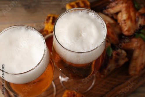 Glasses with beer and delicious baked chicken wings on table, closeup