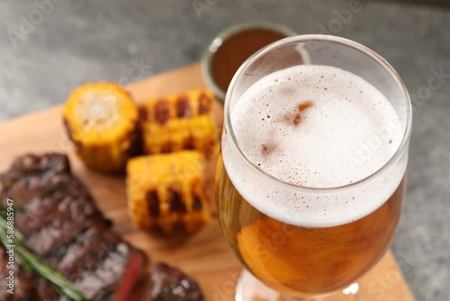 Glass of beer, delicious fried steak and corn on grey table, closeup. Space for text