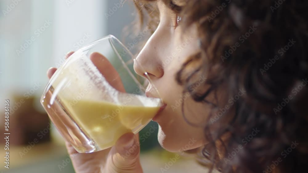 Close up shot of curly haired girl drinking freshly made fruit smoothie from glass and enjoying its taste Close up shot of curly haired girl drinking freshly made fruit smoothie from glass and enjoying its taste