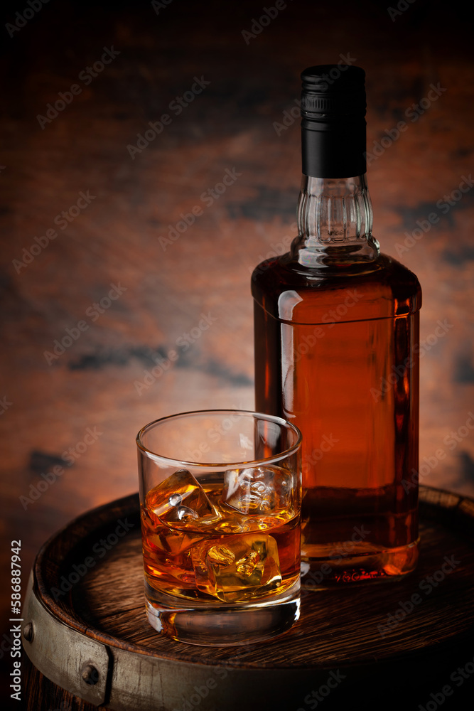 Glass of whiskey with ice cubes and bottle
